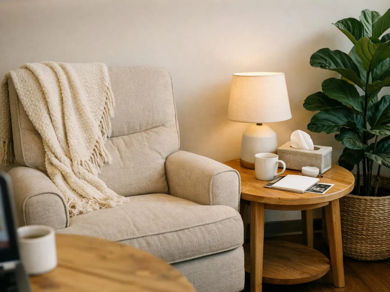 A beige armchair with a throw sits beside a lamp, side table, and potted plant in a cozy room