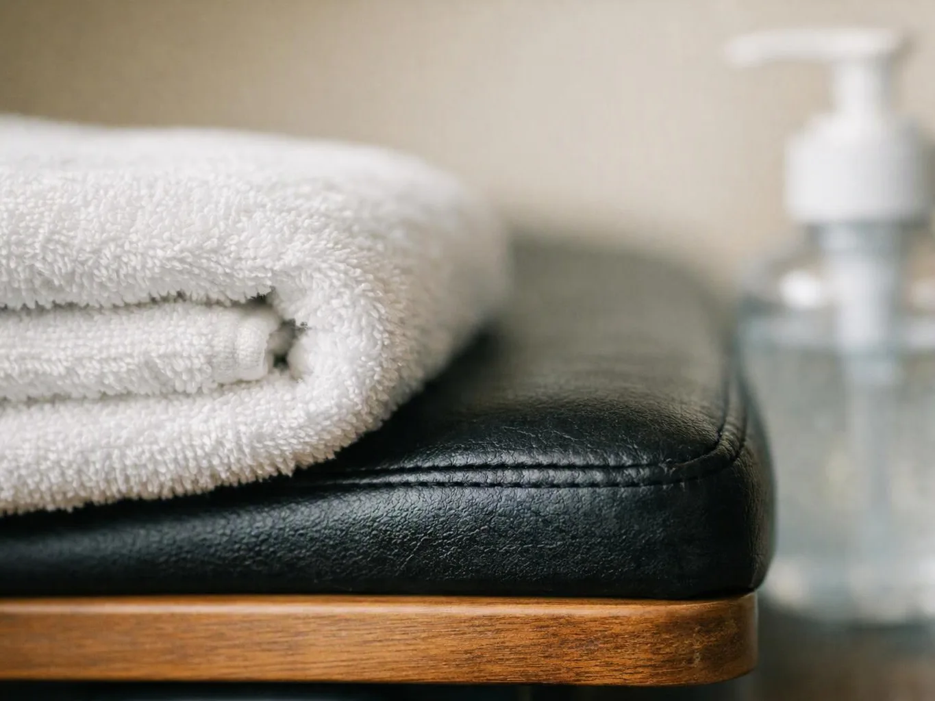 A folded white towel rests on a black leather cushion beside a blurred soap dispenser