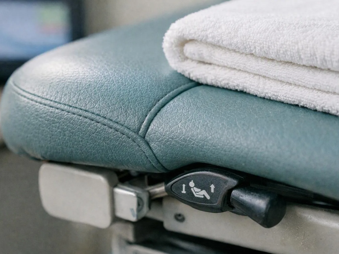 A folded white towel sits on a teal leather chair with an adjustment lever visible underneath